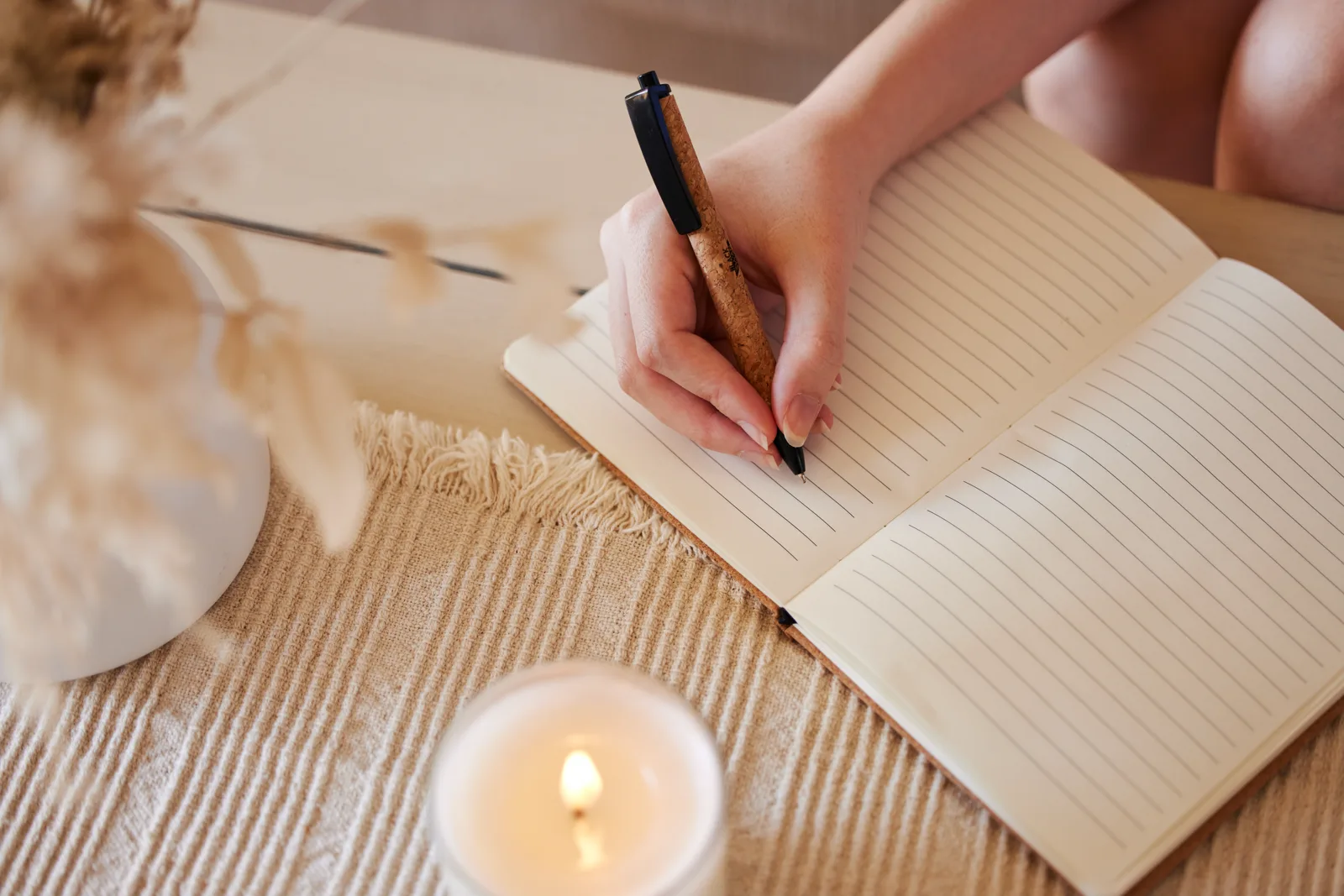 A person writing in a journal by a window with a cup of tea in soft morning light