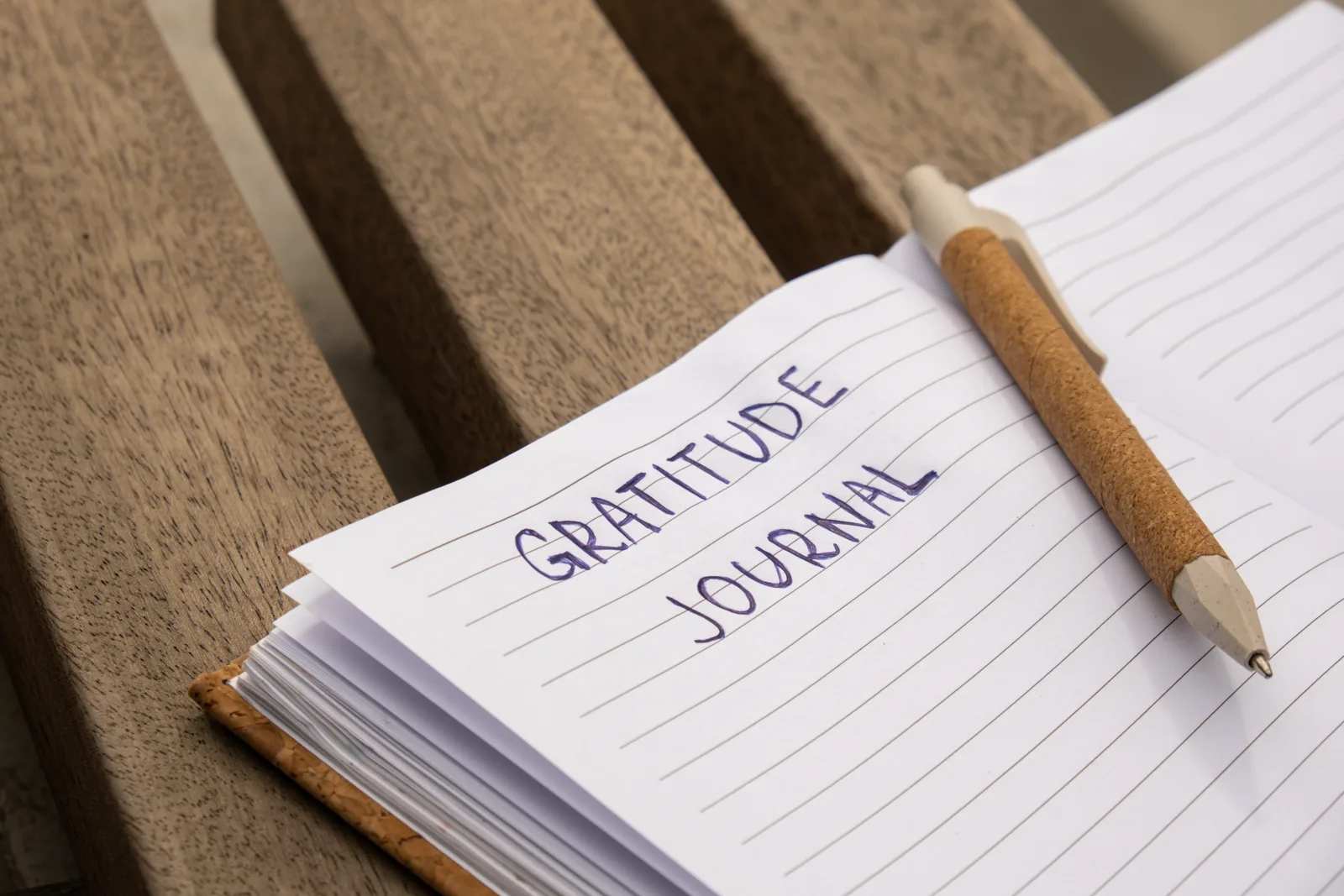A handwritten list on lined paper beside a cup of coffee and a plant, warm daylight