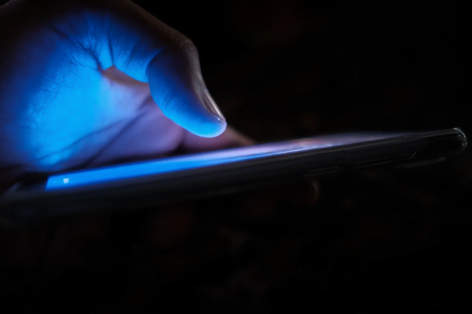 The blue glow of a phone illuminating a hand in an otherwise dark room