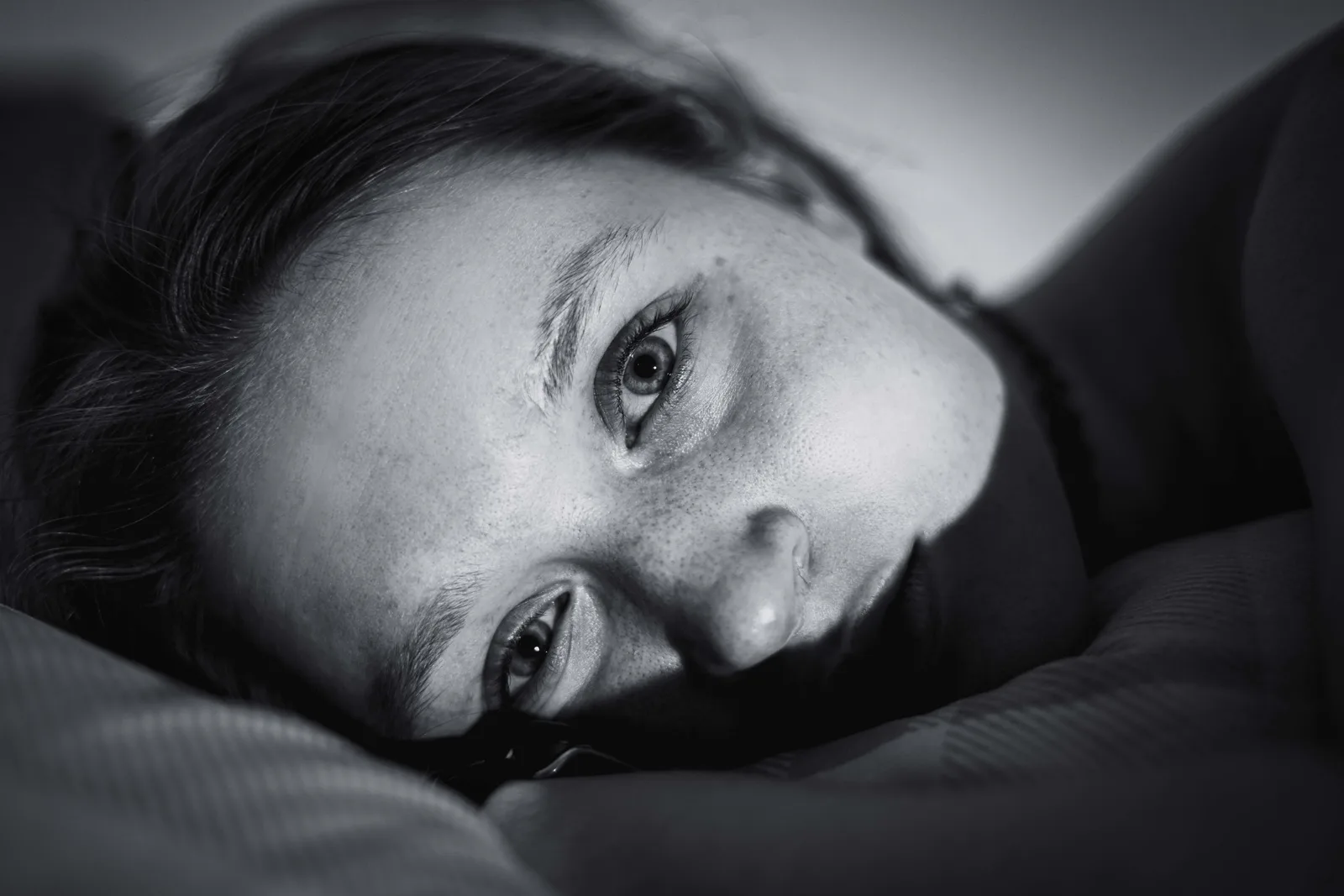 A close-up of a woman's face in low light, awake and lost in anxious thought