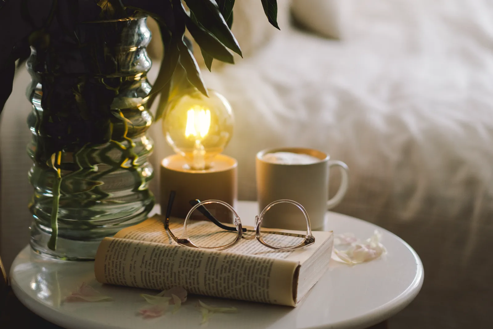 A calm bedside scene with a book, a lamp, and a warm drink, no phone in sight