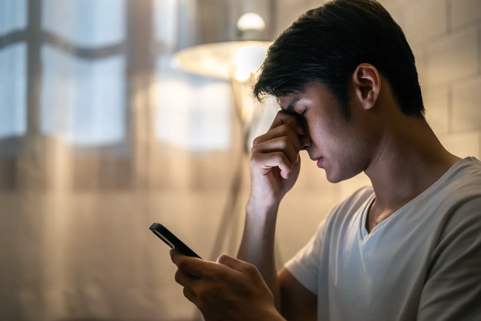 A person looking drained and low while holding a phone, soft grey light