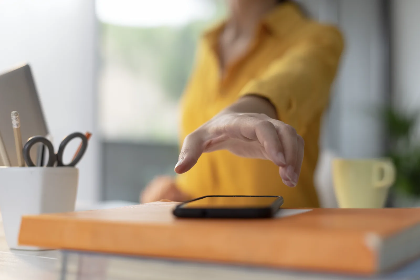 A hand reaching for a phone on a desk mid-task, again