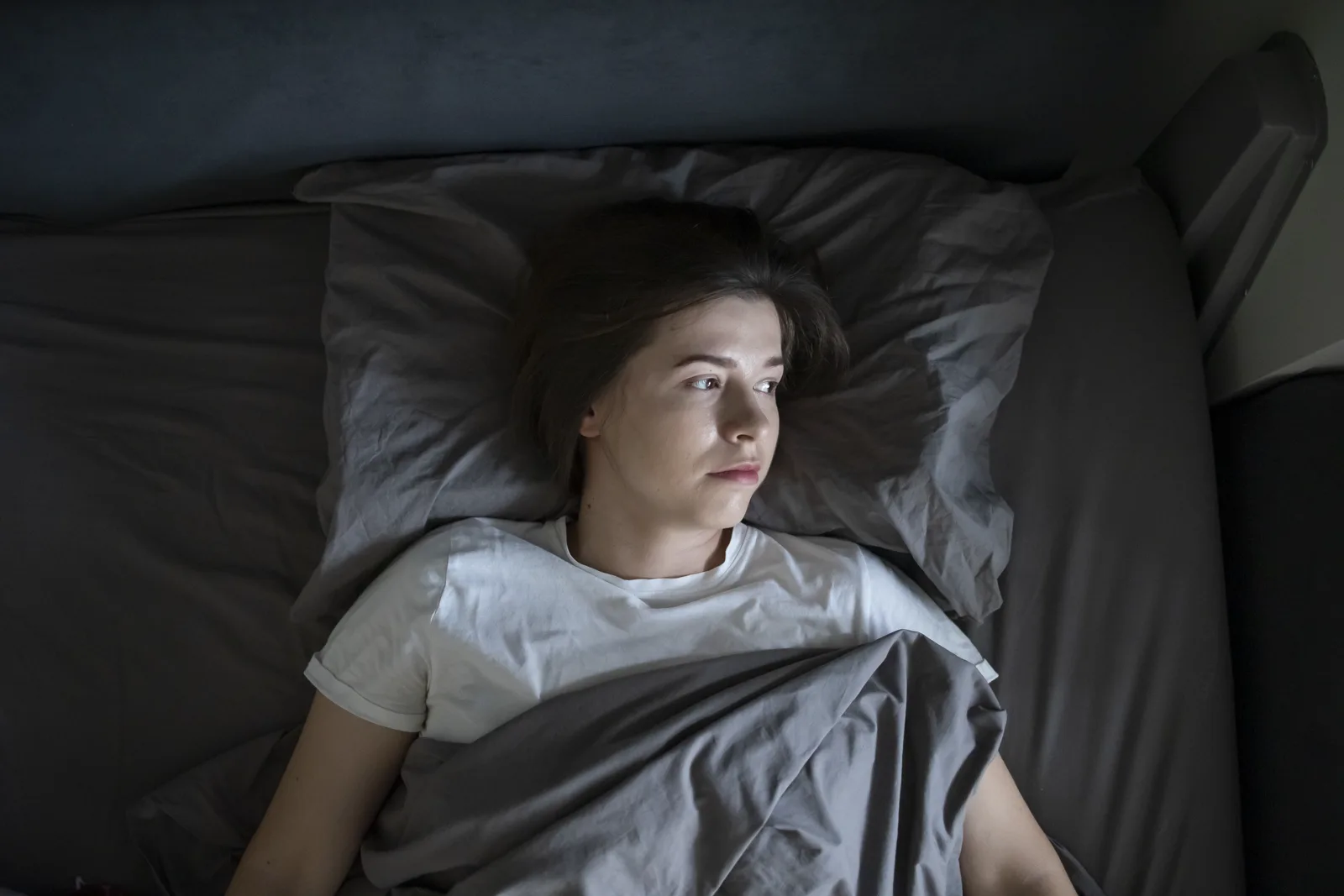 A person lying awake in bed at night, eyes open, unable to sleep
