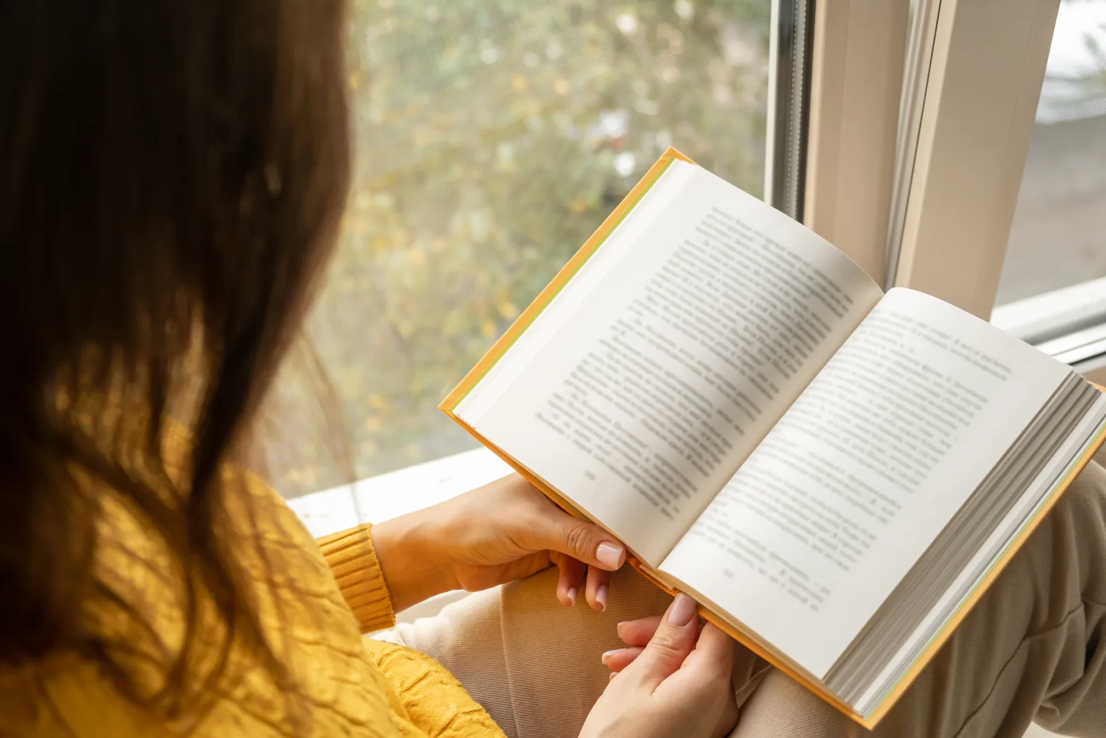 Someone reading a paper book by a window in warm afternoon light